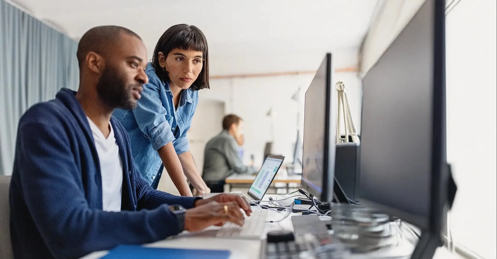 Zwei Personen arbeiten an Computerbildschirmen und analysieren Daten, mit Fokus auf Batteriesysteme, in einem modernen Büro.