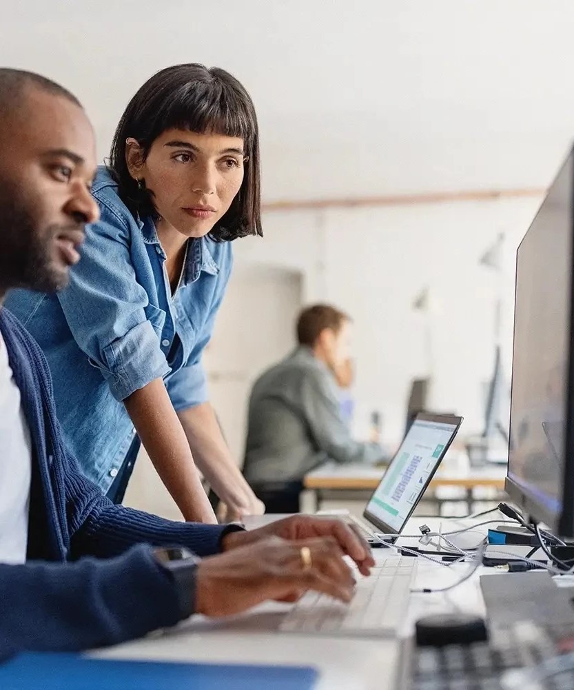 Zwei Personen arbeiten an Computerbildschirmen und analysieren Daten, mit Fokus auf Batteriesysteme, in einem modernen Büro.