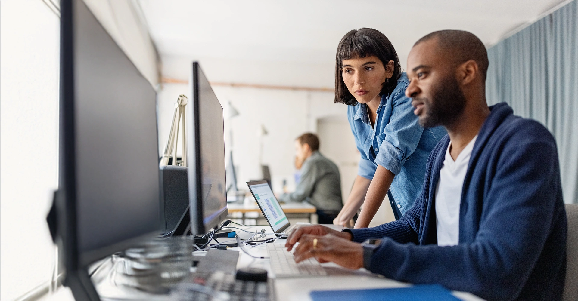 Zwei Personen arbeiten an Computerbildschirmen und analysieren Daten, mit Fokus auf Batteriesysteme, in einem modernen Büro.